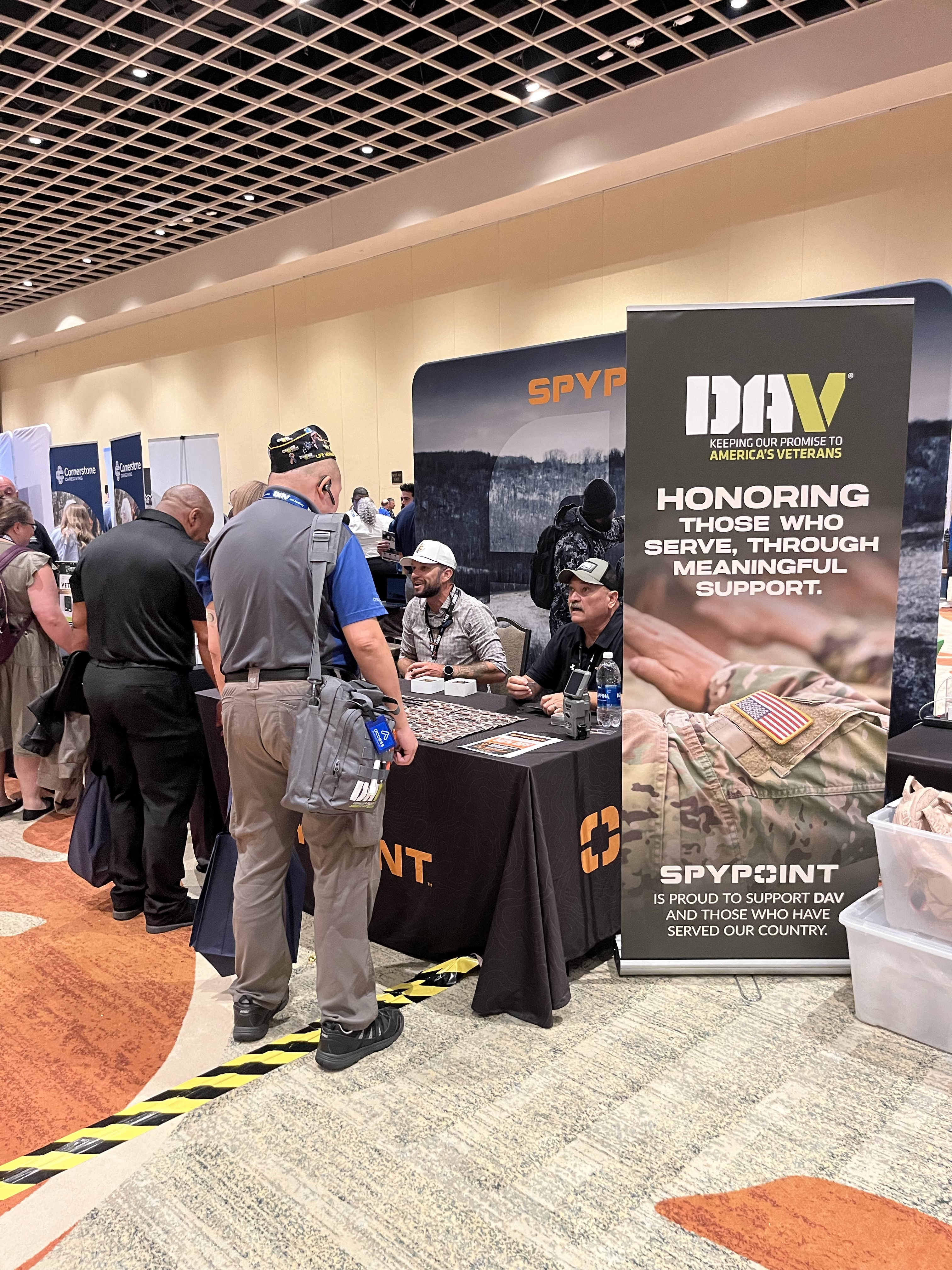 Blog-386_Image-2-SPYPOINT-Booth-at-DAV-National-Convention Veterans visiting the SPYPOINT booth at the 2026 DAV National Convention beside a banner highlighting SPYPOINT support for DAV.