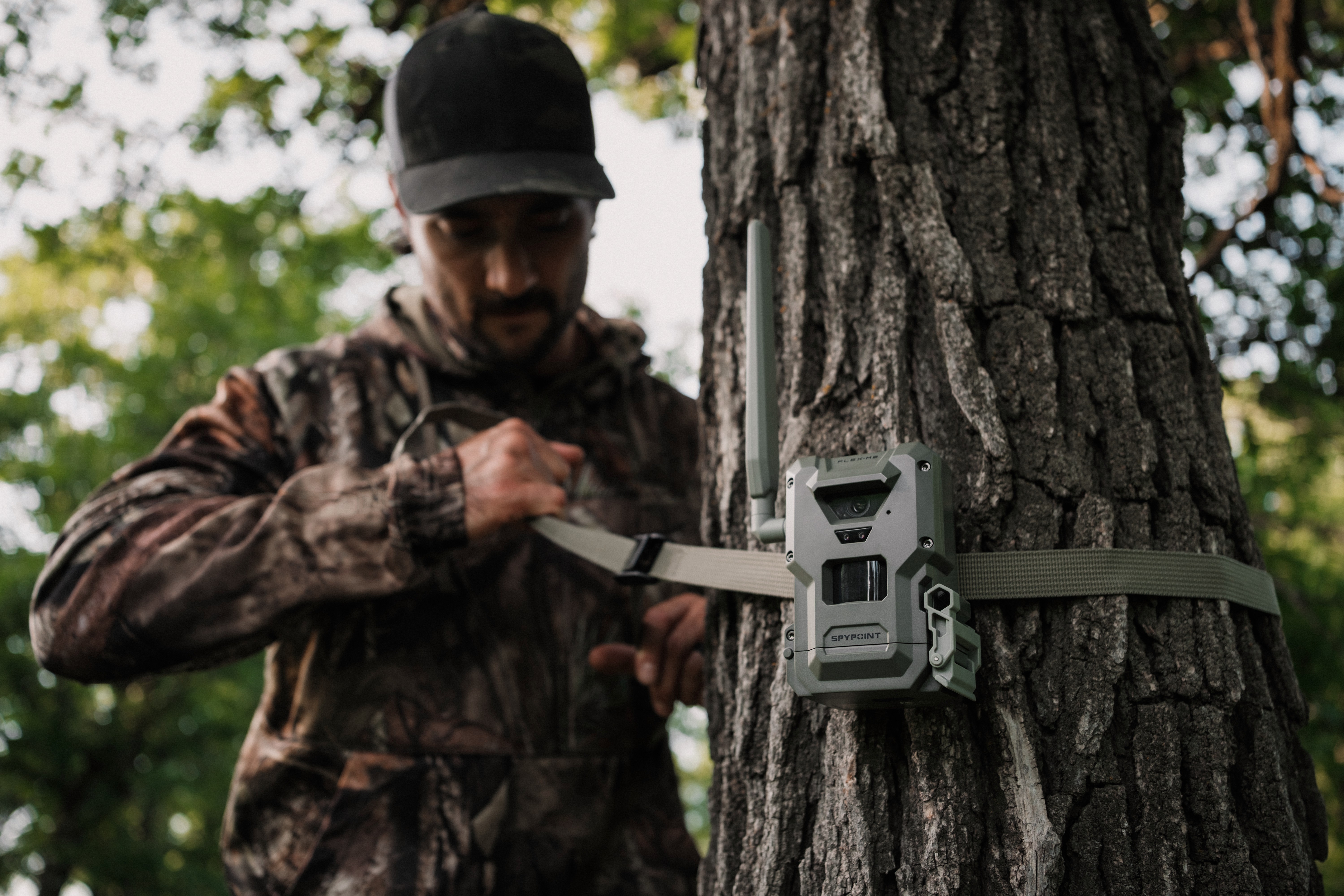 Hunter mounting a SPYPOINT FLEX-M2 cellular trail camera to a tree for remote wildlife scouting.